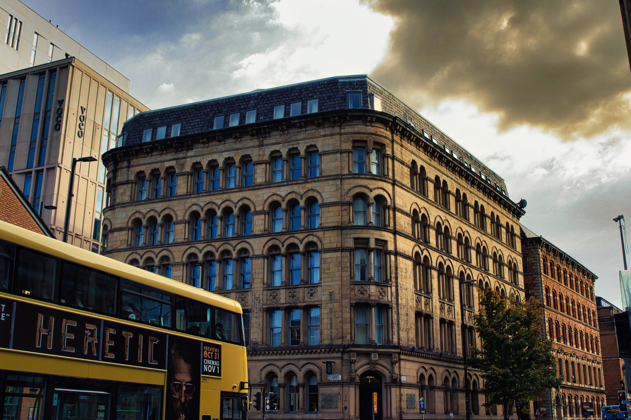 Double-Decker Bus Parked in Front of Stone Building with Many Windows in Manchester, UK.